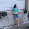 Woman leaning against wall wearing a crop top exposing her belly.