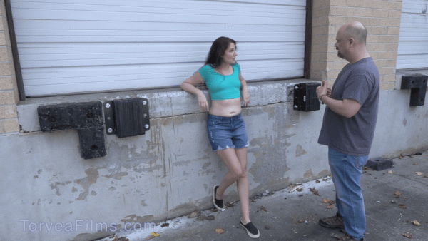 Woman leaning against wall wearing a crop top exposing her belly.